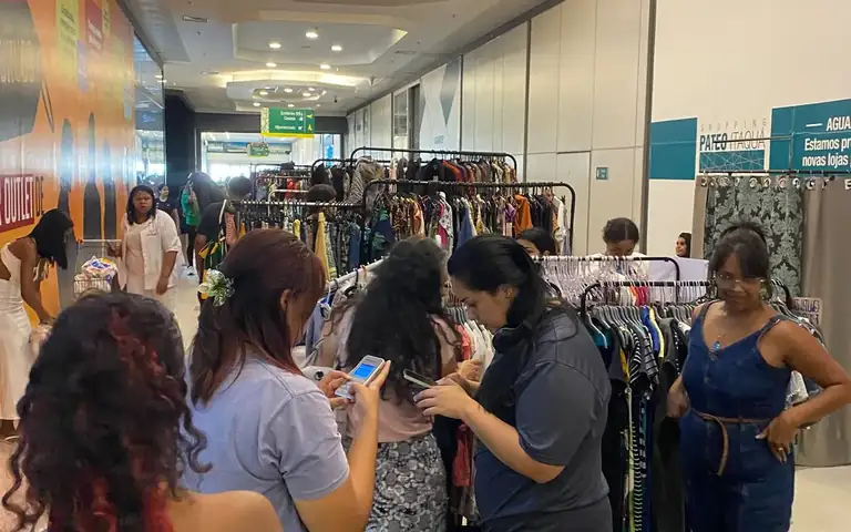 Visitantes circulando entre araras de roupas em feira de brechós